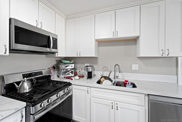 kitchen with appliances with stainless steel finishes, white cabinets, light stone counters, and sink