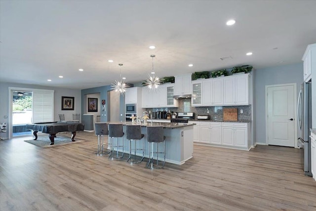 kitchen featuring pool table, hanging light fixtures, an island with sink, stainless steel appliances, and white cabinets