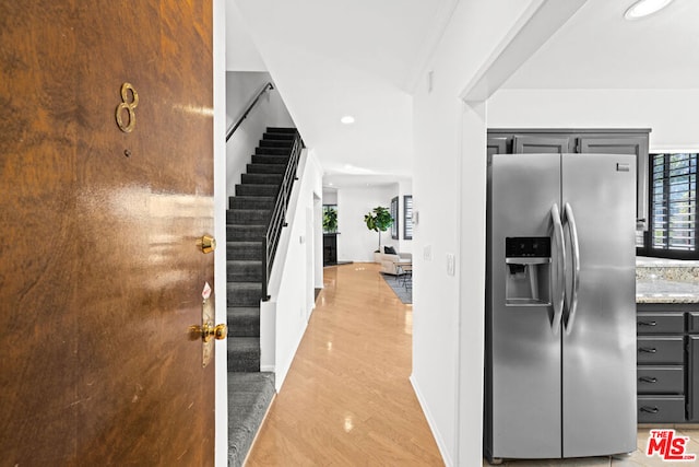 kitchen with light stone counters, gray cabinetry, light wood-type flooring, and stainless steel fridge with ice dispenser