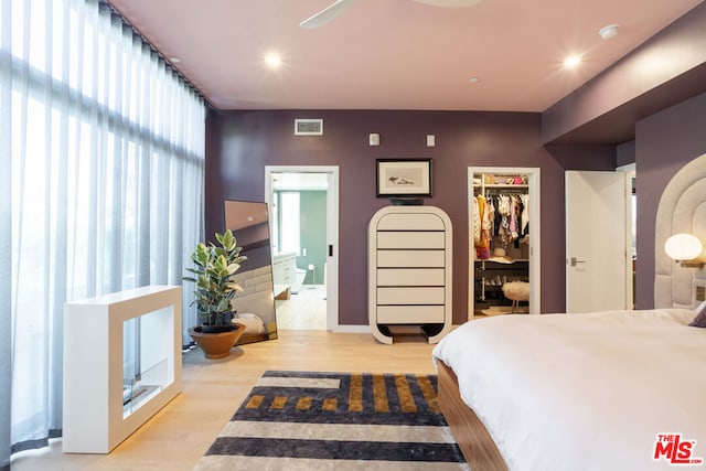 bedroom with ensuite bath, a closet, light wood-type flooring, a walk in closet, and ceiling fan