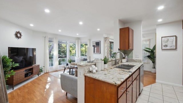 kitchen featuring sink, a center island, light tile patterned floors, dishwasher, and light stone countertops