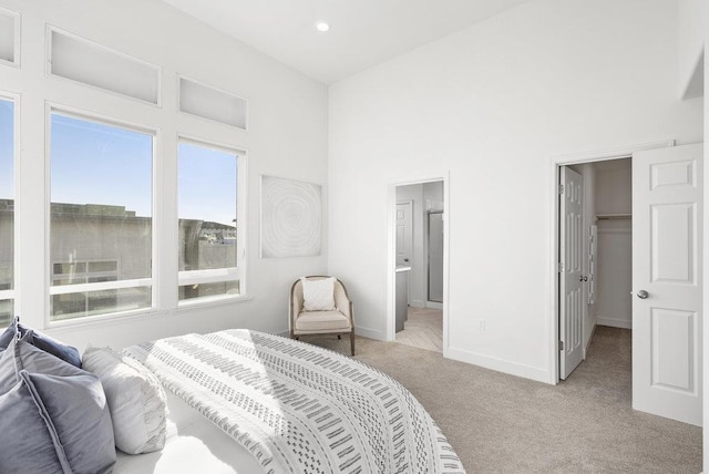 carpeted bedroom featuring a towering ceiling, a walk in closet, a closet, and ensuite bath