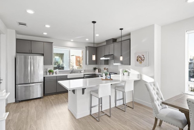 kitchen with kitchen peninsula, hanging light fixtures, a breakfast bar, stainless steel refrigerator, and sink