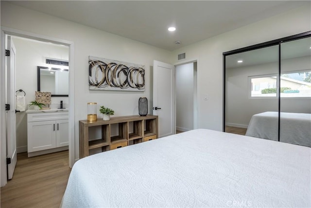 bedroom with ensuite bathroom, sink, a closet, and light wood-type flooring