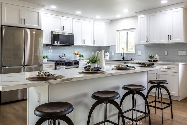 kitchen with sink, appliances with stainless steel finishes, white cabinetry, a kitchen breakfast bar, and a center island