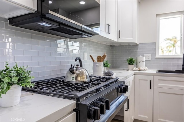 kitchen with tasteful backsplash, range with gas stovetop, light stone countertops, and white cabinets