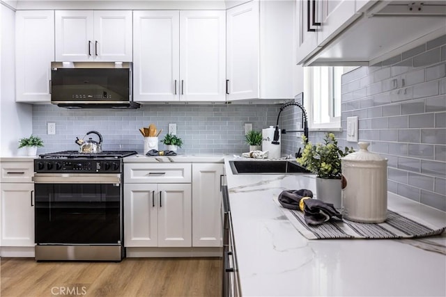 kitchen with sink, white cabinetry, tasteful backsplash, light stone countertops, and gas range oven