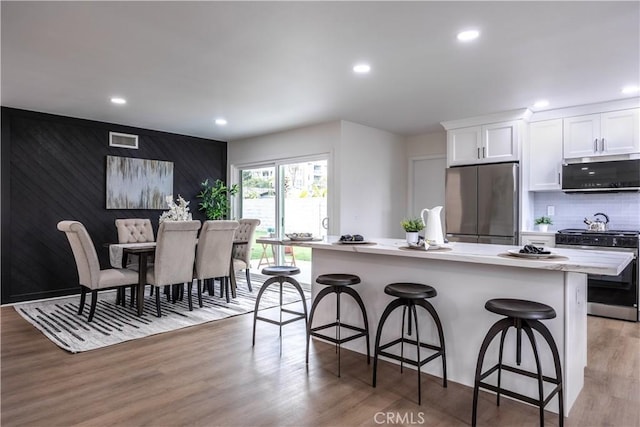 kitchen with white cabinets, a kitchen breakfast bar, a center island, stainless steel appliances, and light wood-type flooring