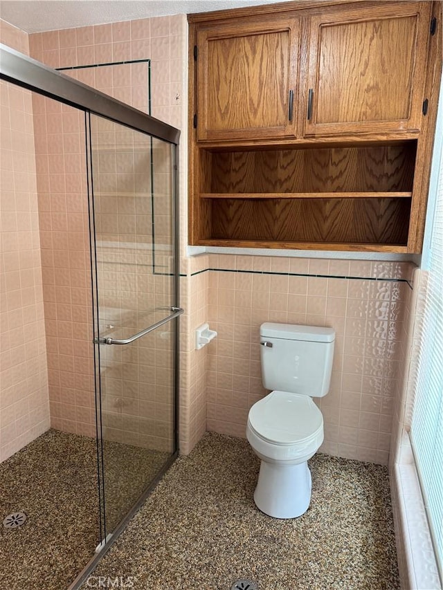 bathroom featuring toilet, tile walls, and a shower with shower door