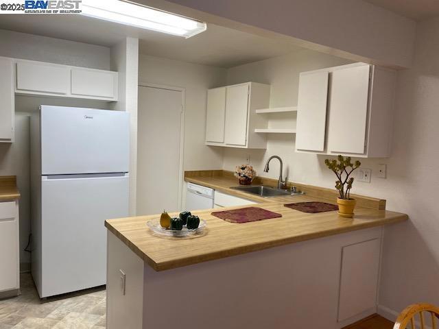 kitchen featuring white appliances, kitchen peninsula, white cabinetry, and sink