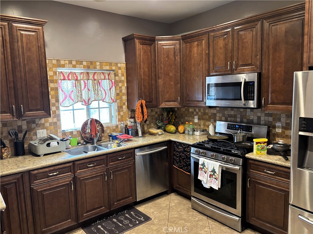 kitchen featuring appliances with stainless steel finishes, tasteful backsplash, sink, and light tile patterned floors