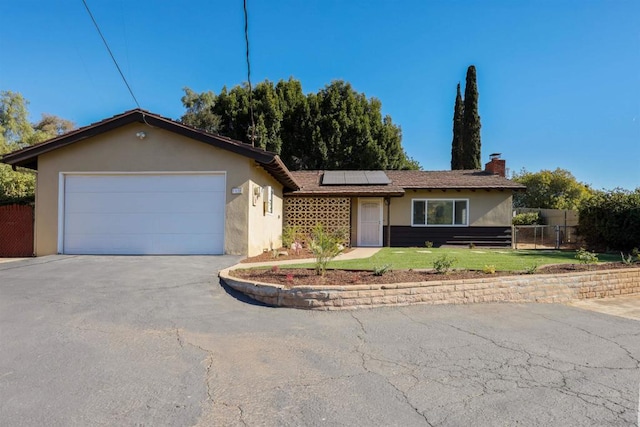 single story home featuring solar panels, a front lawn, and a garage