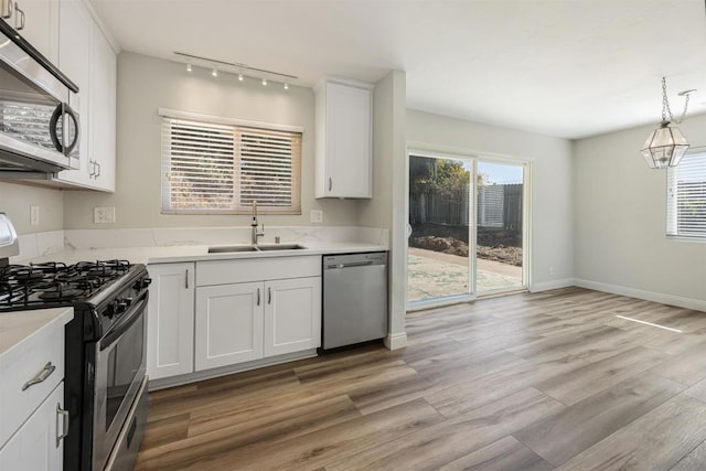 kitchen featuring sink, white cabinetry, light hardwood / wood-style flooring, pendant lighting, and appliances with stainless steel finishes