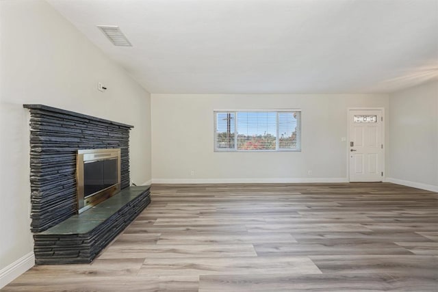 unfurnished living room featuring light wood-type flooring and a stone fireplace