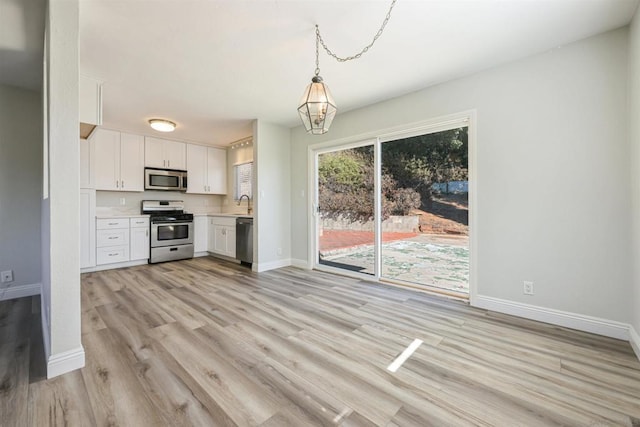 kitchen featuring appliances with stainless steel finishes, light wood-type flooring, white cabinets, decorative light fixtures, and sink