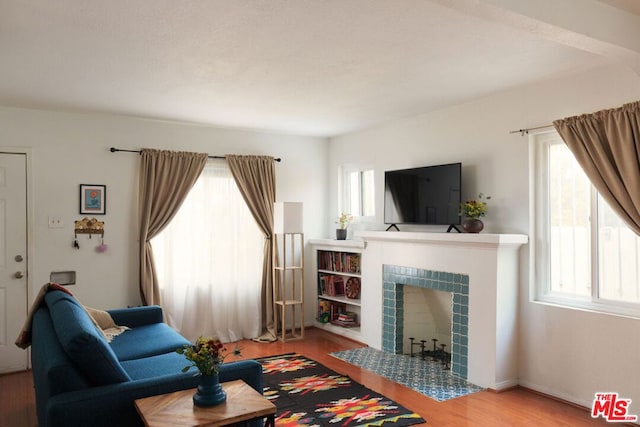 living room featuring wood-type flooring, a tile fireplace, and plenty of natural light