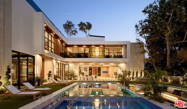 back house at dusk featuring a swimming pool with hot tub, a patio area, and a balcony