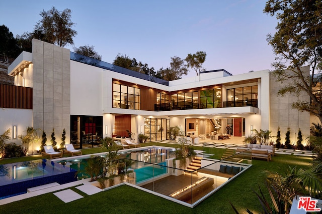 back house at dusk with a swimming pool with hot tub, a patio area, a yard, and a balcony