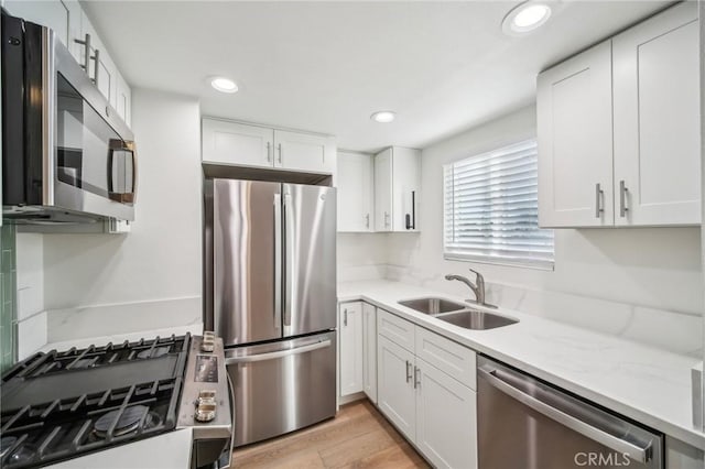 kitchen with white cabinetry, stainless steel appliances, sink, light stone counters, and light hardwood / wood-style flooring