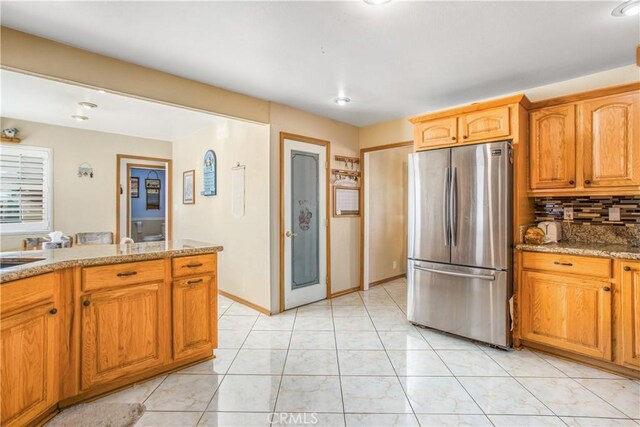 kitchen with stainless steel refrigerator, light stone countertops, light tile patterned floors, and backsplash