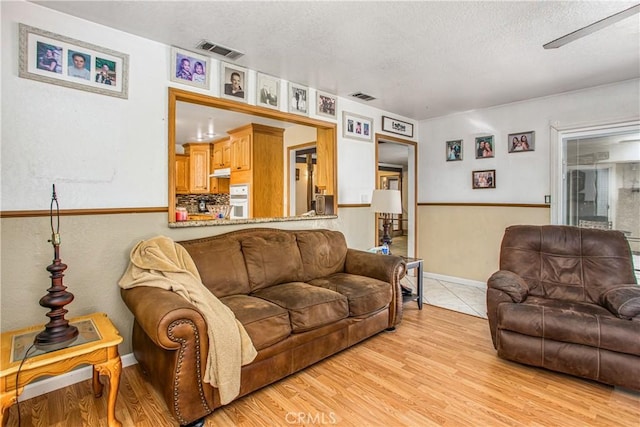 living room with light wood-type flooring, ceiling fan, and a textured ceiling