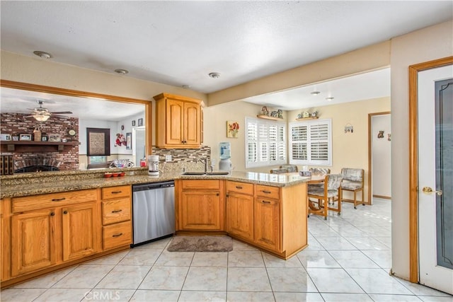 kitchen with sink, stainless steel dishwasher, light stone counters, kitchen peninsula, and a brick fireplace