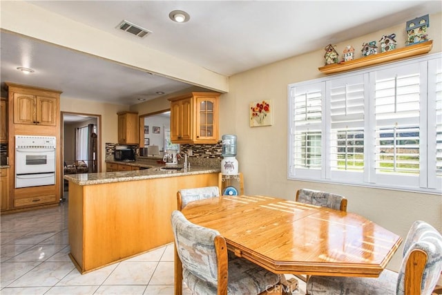 kitchen with sink, white oven, kitchen peninsula, stone counters, and decorative backsplash