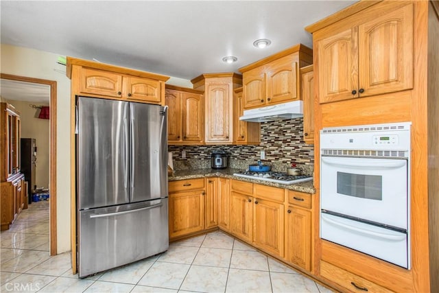 kitchen featuring tasteful backsplash, stone countertops, white gas cooktop, light tile patterned floors, and stainless steel fridge