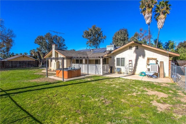 rear view of house with a patio area, a hot tub, solar panels, central AC unit, and a lawn