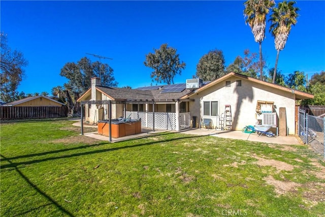 back of property with solar panels, a lawn, a hot tub, central AC, and a patio area