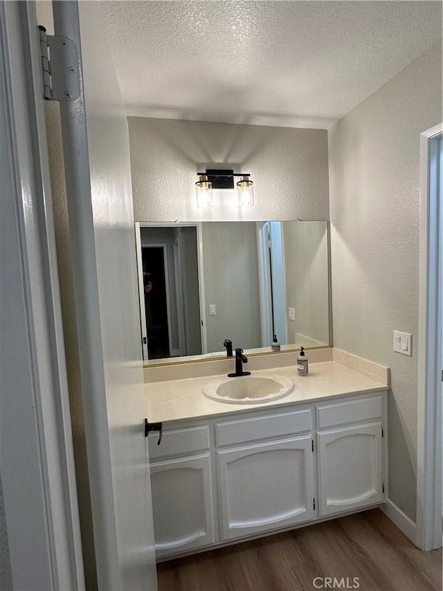 bathroom with a textured ceiling, wood-type flooring, and vanity