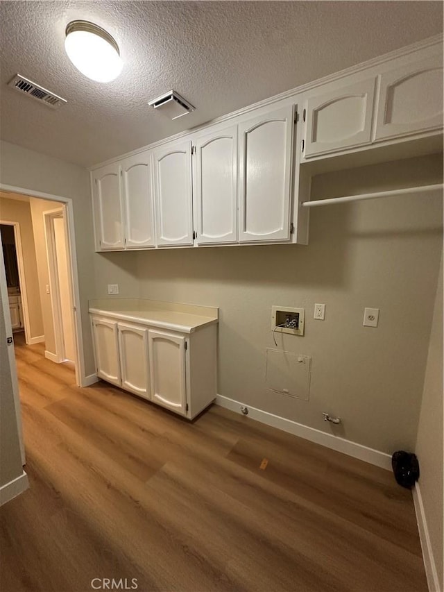 clothes washing area with cabinets, wood-type flooring, hookup for a washing machine, a textured ceiling, and gas dryer hookup