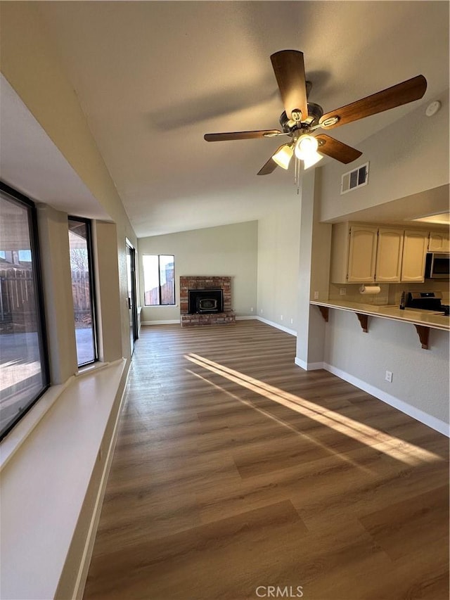 unfurnished living room with ceiling fan, vaulted ceiling, dark hardwood / wood-style floors, and a fireplace