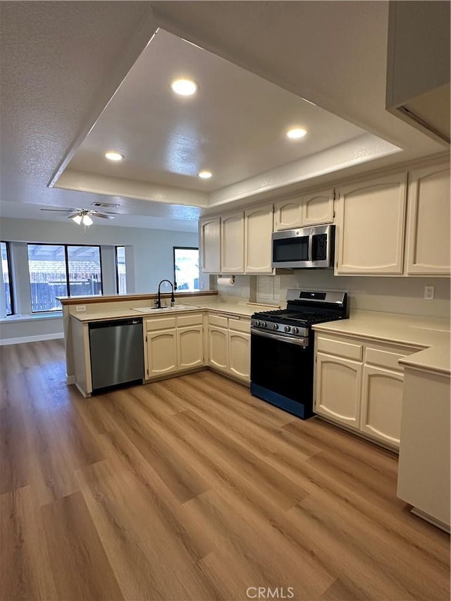 kitchen with stainless steel appliances, white cabinetry, a raised ceiling, and kitchen peninsula