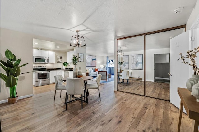 dining space with lofted ceiling, a textured ceiling, light hardwood / wood-style floors, and a notable chandelier