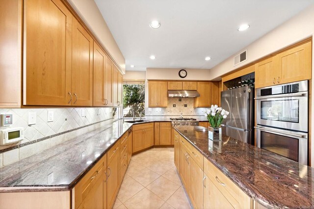 kitchen with stainless steel appliances, dark stone counters, decorative backsplash, a kitchen island, and sink