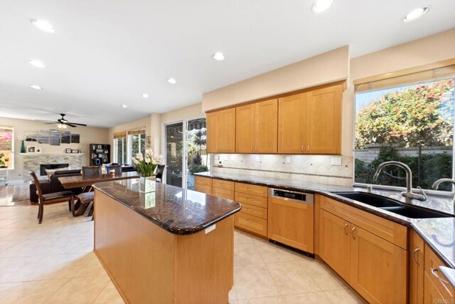 kitchen featuring dishwasher, ceiling fan, dark stone counters, a kitchen island, and sink