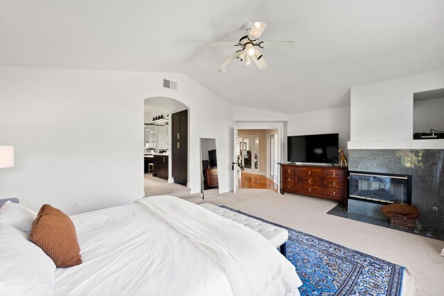 carpeted bedroom featuring lofted ceiling, ensuite bathroom, a tiled fireplace, and ceiling fan