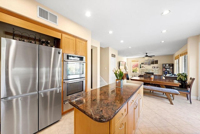 kitchen with stainless steel appliances, dark stone countertops, a kitchen island, ceiling fan, and light tile patterned flooring