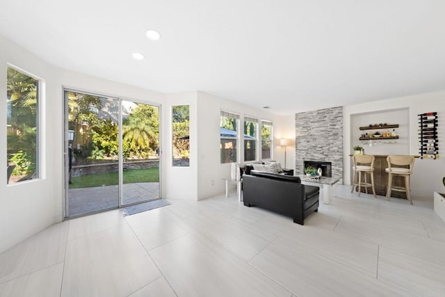 living room with light tile patterned flooring, a wealth of natural light, and a stone fireplace