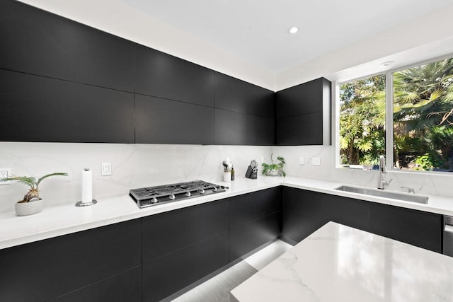 kitchen featuring sink, stainless steel gas cooktop, tasteful backsplash, and light stone counters