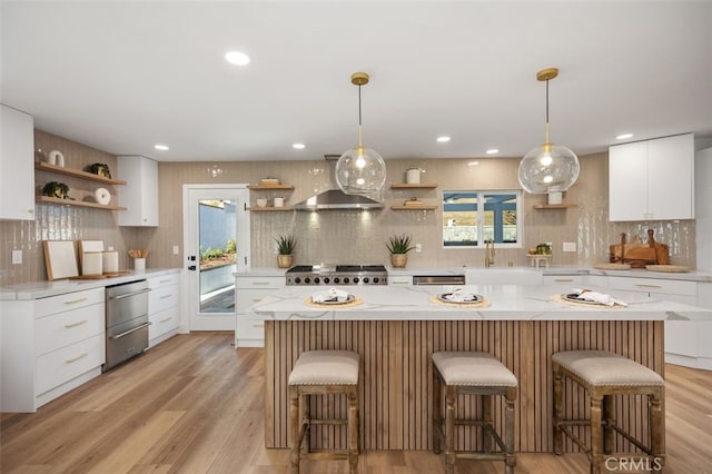 kitchen featuring stainless steel dishwasher, white cabinets, wall chimney range hood, and a center island