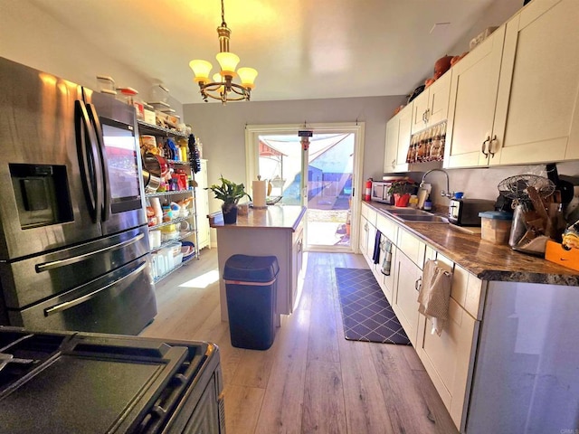 kitchen with appliances with stainless steel finishes, hanging light fixtures, a kitchen island, white cabinets, and sink