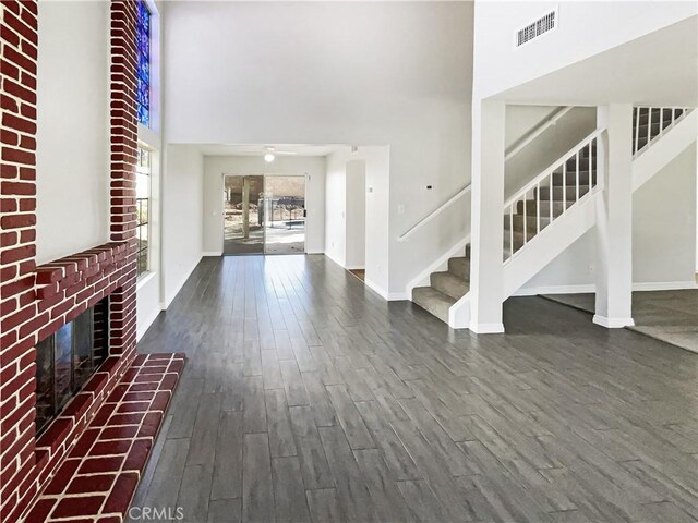 entrance foyer with a towering ceiling, a brick fireplace, ceiling fan, and dark hardwood / wood-style floors