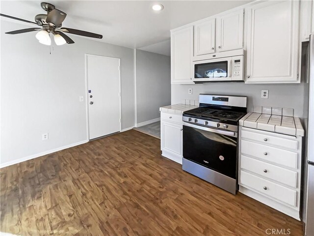 kitchen with stainless steel gas range, tile counters, dark hardwood / wood-style floors, white cabinetry, and ceiling fan