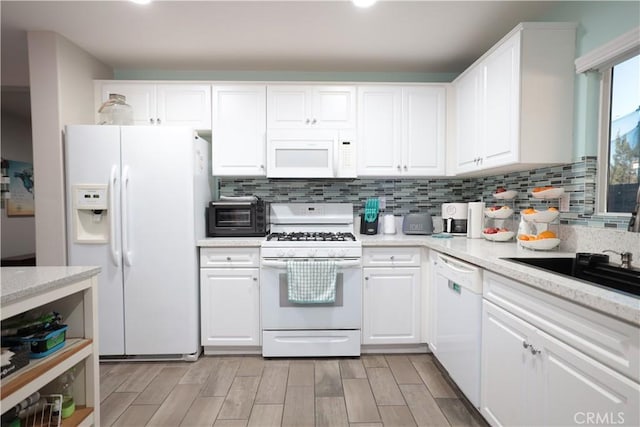 kitchen featuring white appliances, light stone countertops, decorative backsplash, and white cabinets