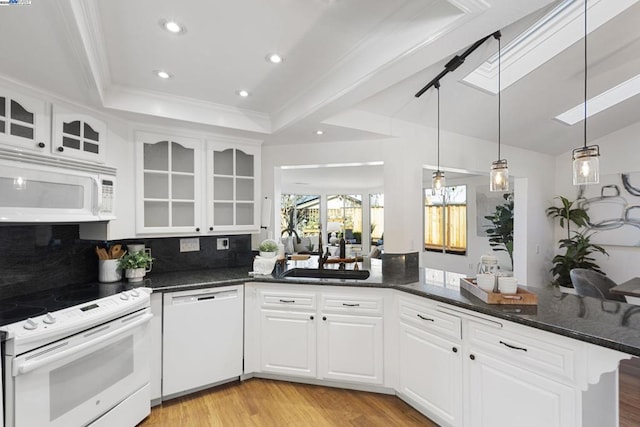 kitchen with white appliances, kitchen peninsula, white cabinets, backsplash, and sink