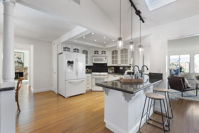 kitchen featuring white appliances, kitchen peninsula, pendant lighting, white cabinets, and a kitchen breakfast bar