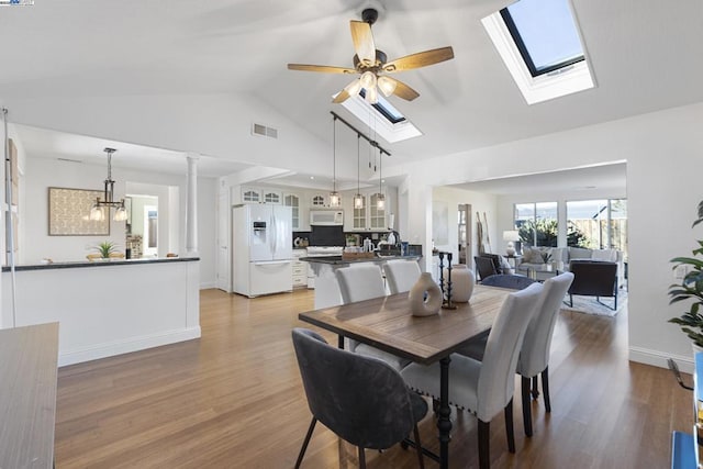 dining area with ceiling fan with notable chandelier, vaulted ceiling with skylight, sink, and light hardwood / wood-style floors