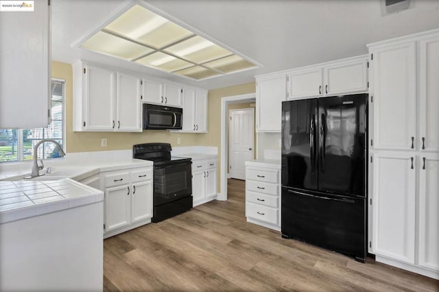 kitchen with sink, white cabinets, light wood-type flooring, tile counters, and black appliances